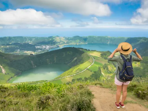 Frau mit Hut und Rucksack genießt den Ausblick auf die Azoren. Perfekte azoren beste reisezeit für dieses Panorama.