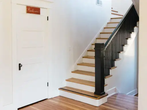 Escalier avec rampe noire, une idée couleur pour une cage d'escalier moderne. Une porte blanche avec un panneau "Restroom" est visible.