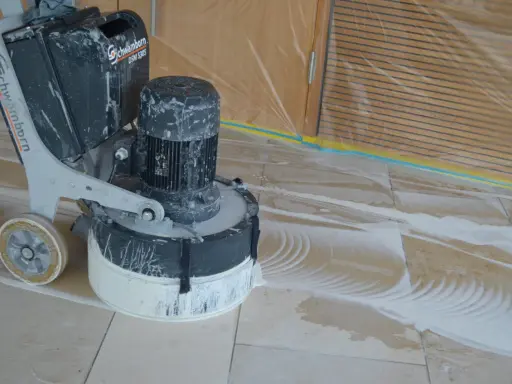 Bodenmaschine poliert Marmor. Staub und Wasser bilden Muster auf dem Boden, während die Maschine den Stein glänzend macht.