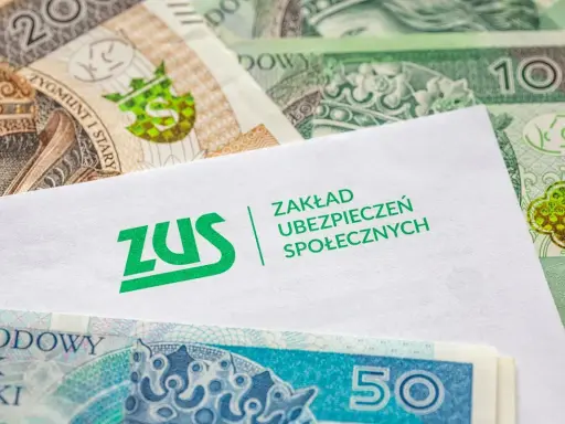 Koperta z logo ZUS leży na stosie polskich banknotów. z15b druk.