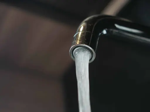 Un robinet chromé verse un jet d'eau. L'image évoque la dureté de l'eau par commune en France, un sujet important pour la vie quotidienne.