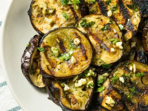 Aubergines grillées en rondelles, garnies d'ail et de persil, sur une assiette.
