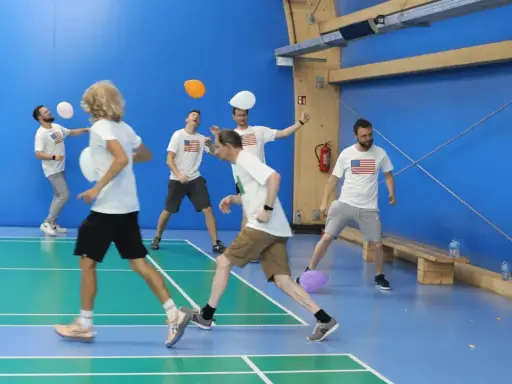Mężczyźni w koszulkach z amerykańską flagą grają w gry zespołowe dla dorosłych, odbijając balony na hali sportowej.