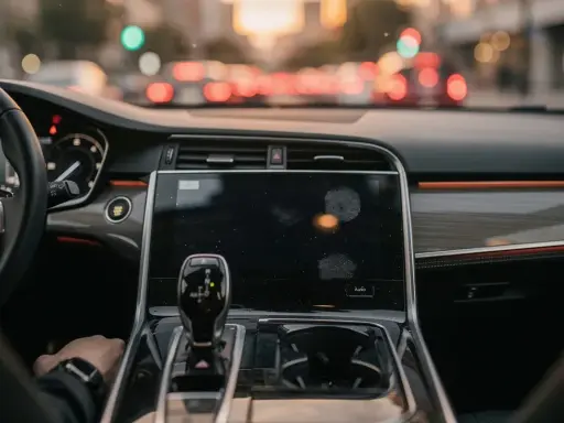 Interno di un'auto moderna, con cambio automatico e schermo touch. La mano del guidatore è sul cambio, pronto per un viaggio in **auto hold golf**.