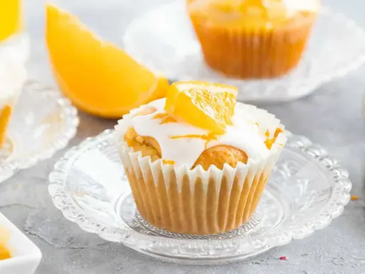 Fanta Muffins mit weißer Glasur und Orangenspalten, serviert auf kleinen Glastellern.