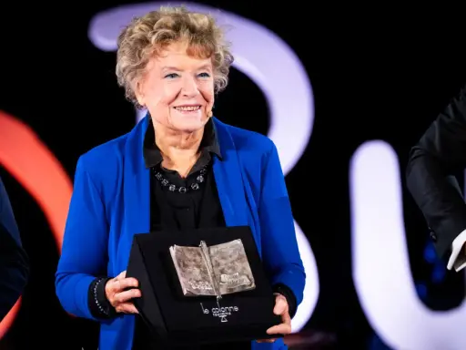 Una donna sorride sul palco, tenendo un premio a forma di libro aperto. Un simbolo di ispirazione per le libere donne.