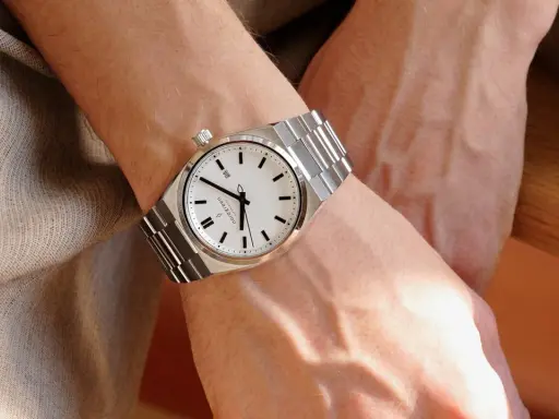 En person bär en silverfärgad klocka med vit urtavla på vänster handled. Vilken arm har man klockan på?
