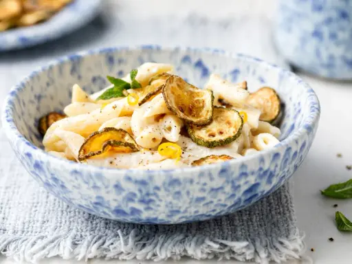 Piatto di pasta cremosa con ricotta e zucchine croccanti, guarnito con scorza di limone e menta.
