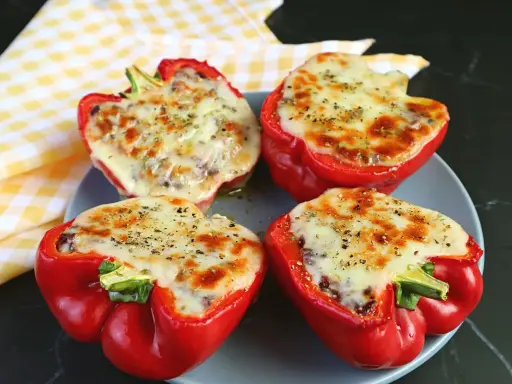 Quattro peperoni ripieni in friggitrice ad aria, con formaggio fuso e spezie, pronti per essere gustati.