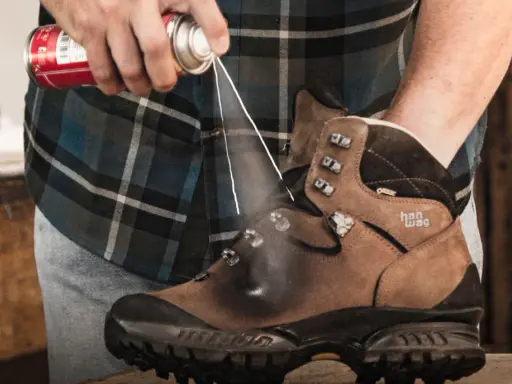 Jak zabezpieczyć nowe buty skórzane? Mężczyzna spryskuje brązowe buty trekkingowe preparatem ochronnym.