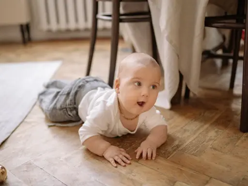 Maluch na podłodze, ćwiczący czworakowanie a raczkowanie, z zaciekawieniem patrzy w bok.