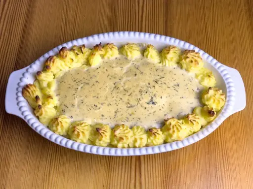 En gratinerad fiskrätt med alaska pollock recept, omgiven av spritsad potatis.