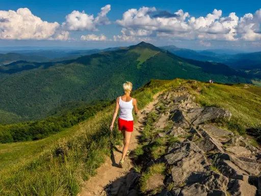 Kobieta wędruje szlakiem pośród zielonych wzgórz. Bieszczady jakie to góry – rozległe, malownicze, z dalekimi horyzontami.