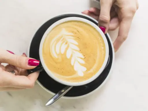 Une main tient une tasse de café latte avec un dessin de feuille. Un guide pour comment faire un latte parfait.
