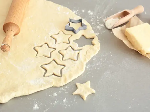 Plätzchenteig zu krümelig? Sterne werden ausgestochen. Teig, Nudelholz, Butter und Mehl sind bereit für leckere Kekse.