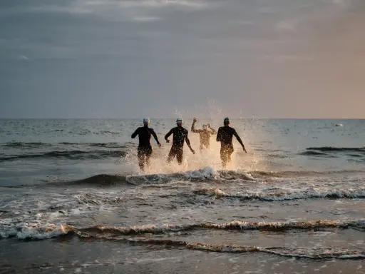 Vier Schwimmer stürmen ins Meer. Die durchschnittliche Zeit für 1km schwimmen wird hier wohl im Wettkampf ermittelt.