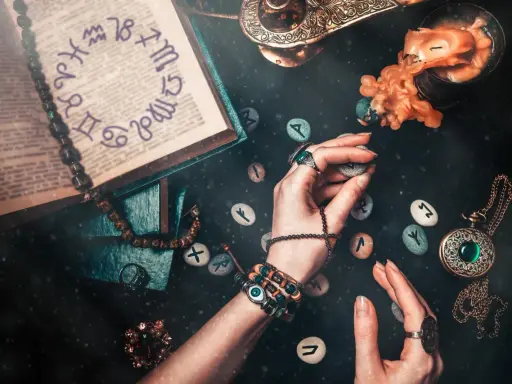 Ręce trzymają kamienie z runami, obok księga z symbolami zodiaku. To wszystko sugeruje, że godzina urodzenia numerologia może być kluczem do odczytania przyszłości.