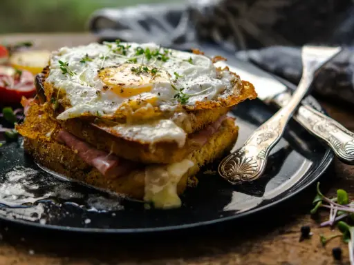 Un croque-madame gourmand, un des plats typiques parisiens, avec un œuf au plat, jambon et fromage fondant, servi avec des tomates et des pousses.