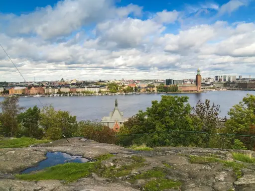 Vy över Riddarfjärden från Skinnarviksberget Stockholm, med Stadshuset i bakgrunden under en molnig himmel.