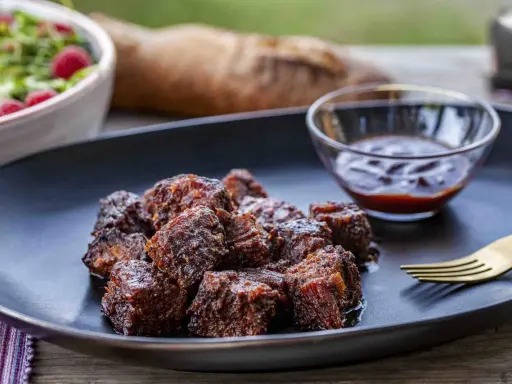Saftige, karamellisierte **burnt ends** auf einem Teller mit BBQ-Sauce und Salat. Ein Fest für Fleischliebhaber!