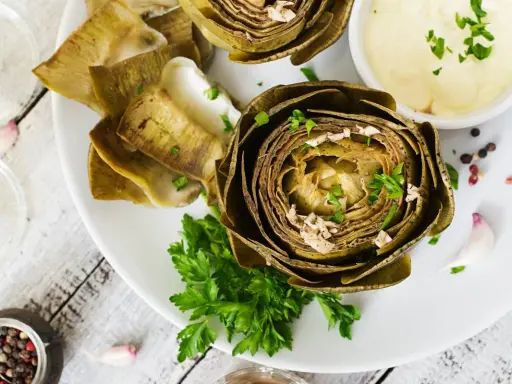 Deliciosas alcachofas al horno, tiernas y doradas, servidas con una cremosa salsa y perejil fresco. Un plato perfecto para disfrutar.