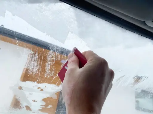 Dłoń zeskrobuje szron na szybie, odsłaniając fragmenty drewnianej elewacji. Zima daje się we znaki.
