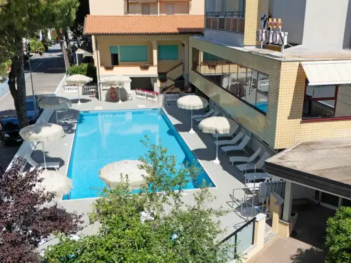 Piscina invitante e lettini prendisole al **hotel Simon Gatteo Mare**. Ombrelloni bianchi e vegetazione rigogliosa creano un'oasi di relax.