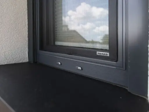 Szary parapet zewnętrzny pod oknem z moskitierą. Zastanawiasz się, czym przykleić parapet zewnętrzny blaszany?