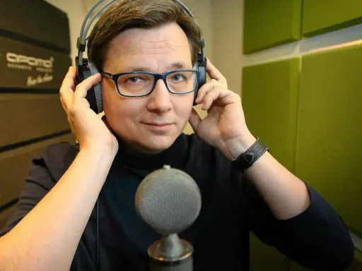 Mężczyzna w słuchawkach i okularach, gotowy do nagrania. Może to lektor porno, a może czyta bajki.