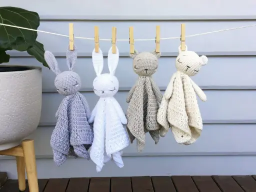 Cuatro adorables mantas de apego crochet, con forma de conejitos y ositos, cuelgan de una cuerda.