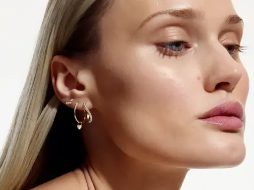 Delikatne kolczyki z kwiatami i serduszkiem, zdobiące ucho modelki, dodają subtelnego blasku.