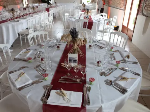 Une table dressée à la française, prête pour un événement. Nappes blanches, chemins de table bordeaux, vaisselle et couverts élégants, et une touche champêtre avec des épis de blé et de la lavande.