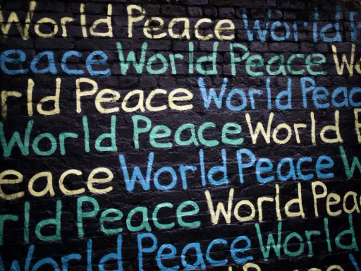 Un promemoria di Gianni Rodari: "Pace nel mondo" scritto in giallo, blu e verde su un muro di mattoni neri.