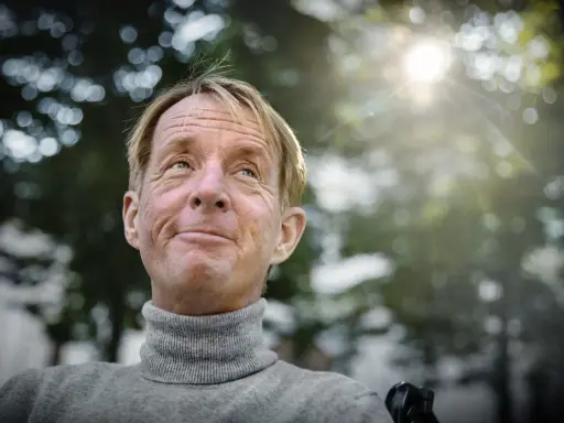 En leende man med rullstol, kanske en scen från filmer med Nils Hallberg, tittar upp mot solen.