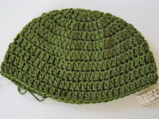 Gorro de lana verde tejido a mano, ideal para aprender como tejer un gorro de lana para principiantes. Cinta métrica al lado.