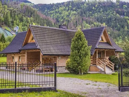 Drewniana bacówka pod skocznią, otoczona zielenią, z widokiem na górskie zbocza.