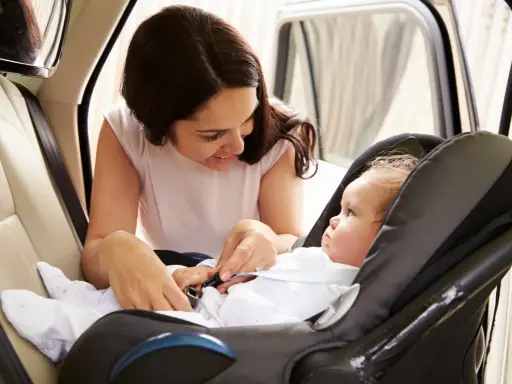 Madre abrochando el cinturón de seguridad a su bebé en la silla del coche. Los niños en el coche viajan seguros.