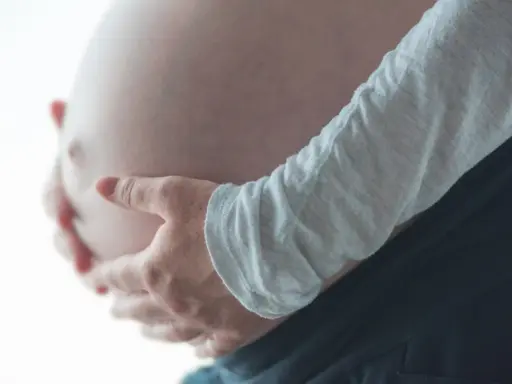 Dłonie obejmujące ciążowy brzuch, odczuwając ucisk na pęcherz w ciąży w II trymestrze.