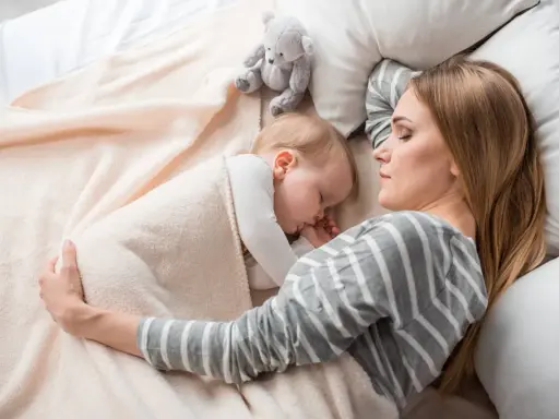 Mamma e bimbo dormono abbracciati, un tenero momento di co sleeping con un orsetto di peluche.