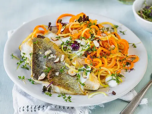 Gebratenes Fischfilet mit Spiralnudeln aus Karotten und Zucchini, garniert mit Kräutern und Mandelsplittern. Perfekt für leichte fasten rezepte.