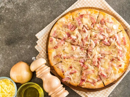 Flammekueche gourmande, garnie de lardons et d'oignons sur une base de fromage blanc crémeux. Un délice croustillant.