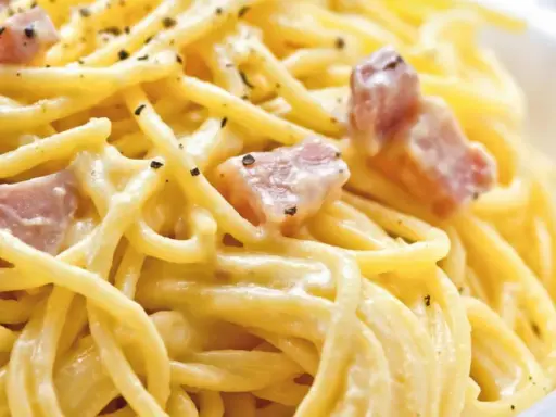 Cremige Spaghetti Carbonara, nur mit Eigelb zubereitet, garniert mit Speckwürfeln und schwarzem Pfeffer.