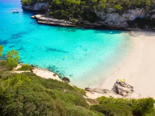 Traumhafte mallorca buchten mit türkisfarbenem Wasser, weißem Sand und grünen Pinien. Ein Boot ankert im Meer, eine Rettungsschwimmerturmbefindet sich am Strand.
