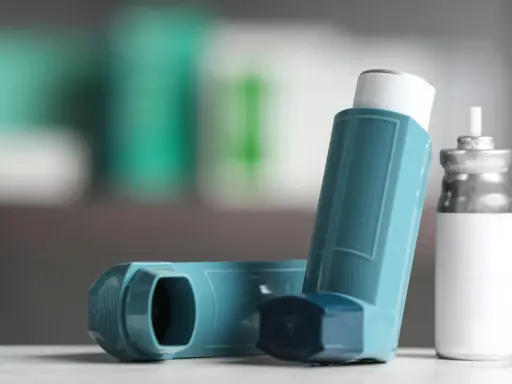 Zwei Inhalatoren, einer davon ein Symbicort-Spray, liegen auf einer weißen Oberfläche.