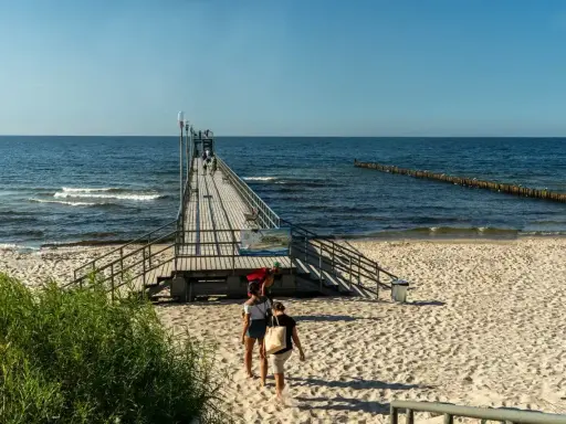 Sianożęty atrakcje: drewniane molo wchodzi w morze, plaża i fale.