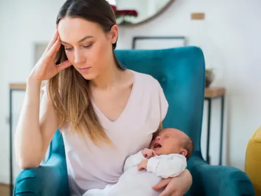 Zmęczona mama z płaczącym niemowlakiem na rękach, w fotelu, w poszukiwaniu siebie.