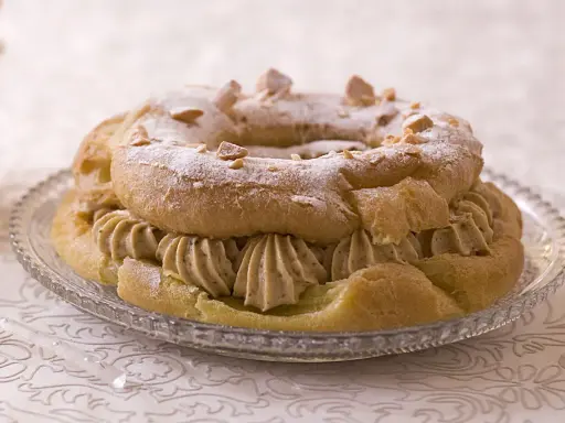 Bûche façon Paris-Brest, une couronne de pâte à choux garnie de crème onctueuse et saupoudrée de sucre glace et d'amandes effilées.