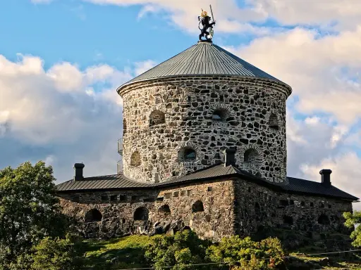 Skansen Lejonet, ett stendäckat torn med en gyllene lejonstaty på toppen, reser sig mot en molnig himmel.
