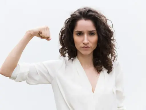 Kobieta pokazuje biceps, symbolizując siłę. Może to być metafora objawów wysokiego testosteronu, takich jak pewność siebie i determinacja.