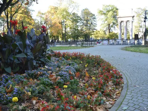 Jesienny park strzelecki Tarnów. Kolorowe rabaty kwiatowe i liście na brukowanej ścieżce.